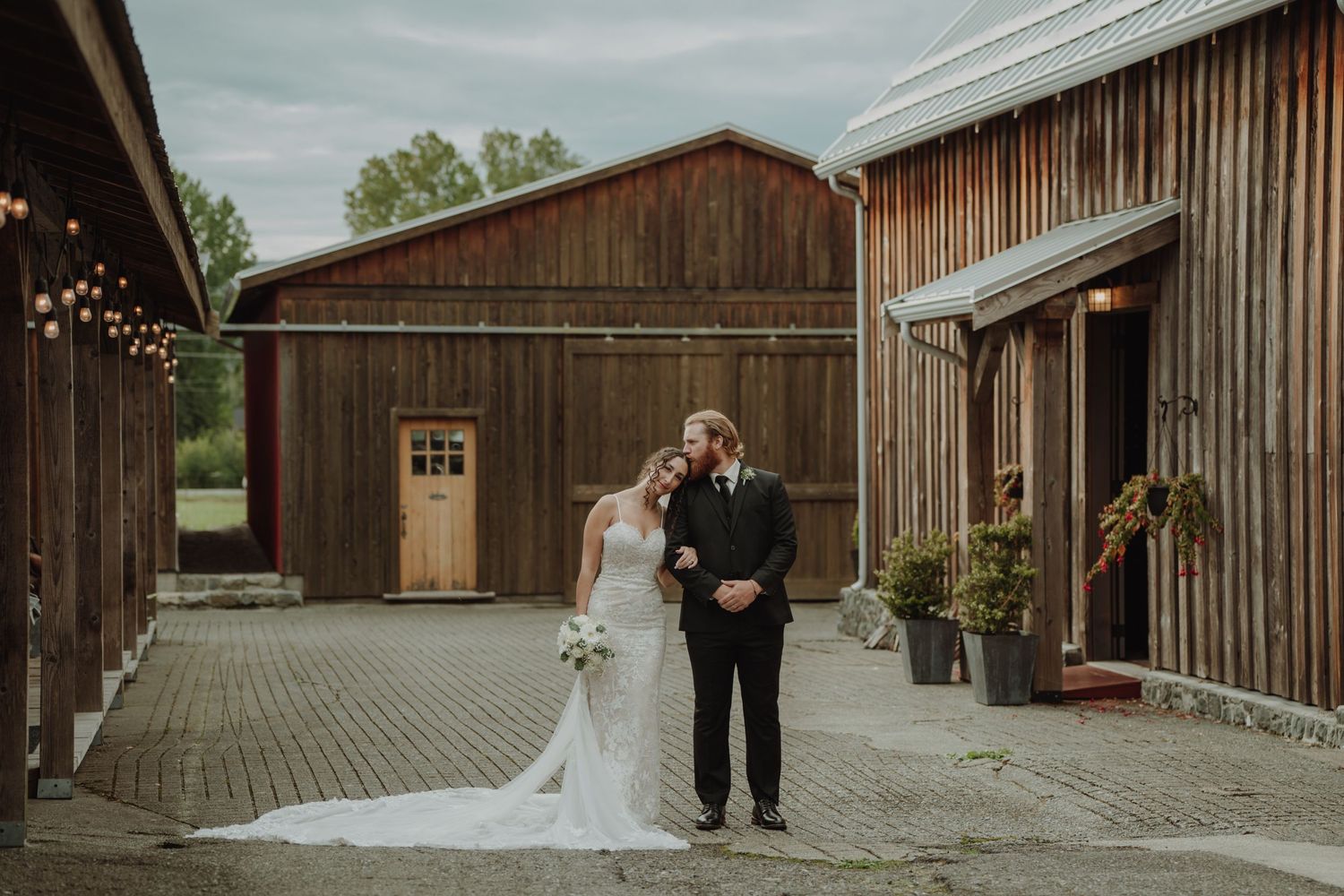 Bride and groom share romantic moment outside rustic wooden barn wedding venue.