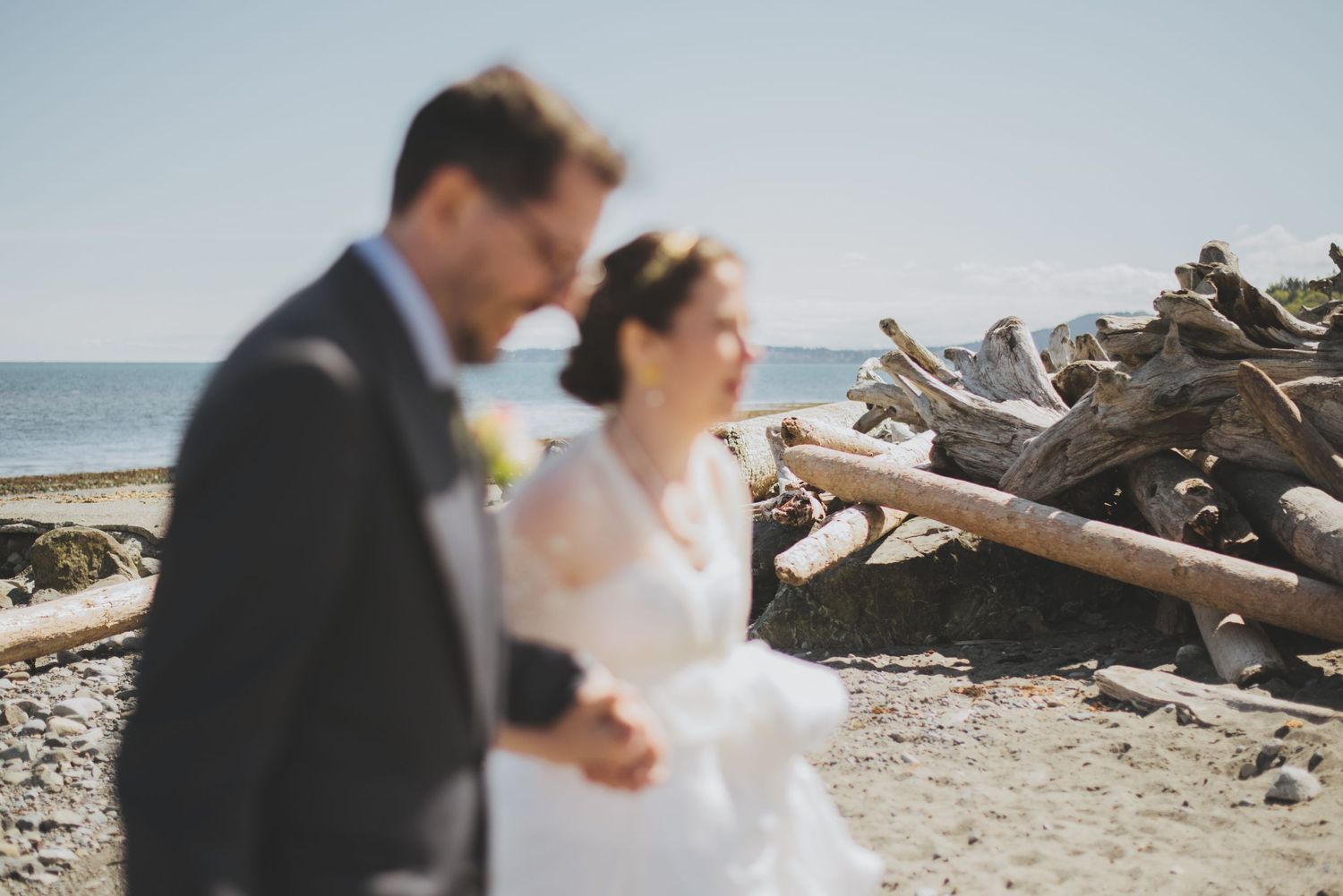 A wedding couple walks along a driftwood-strewn beach on their special day.