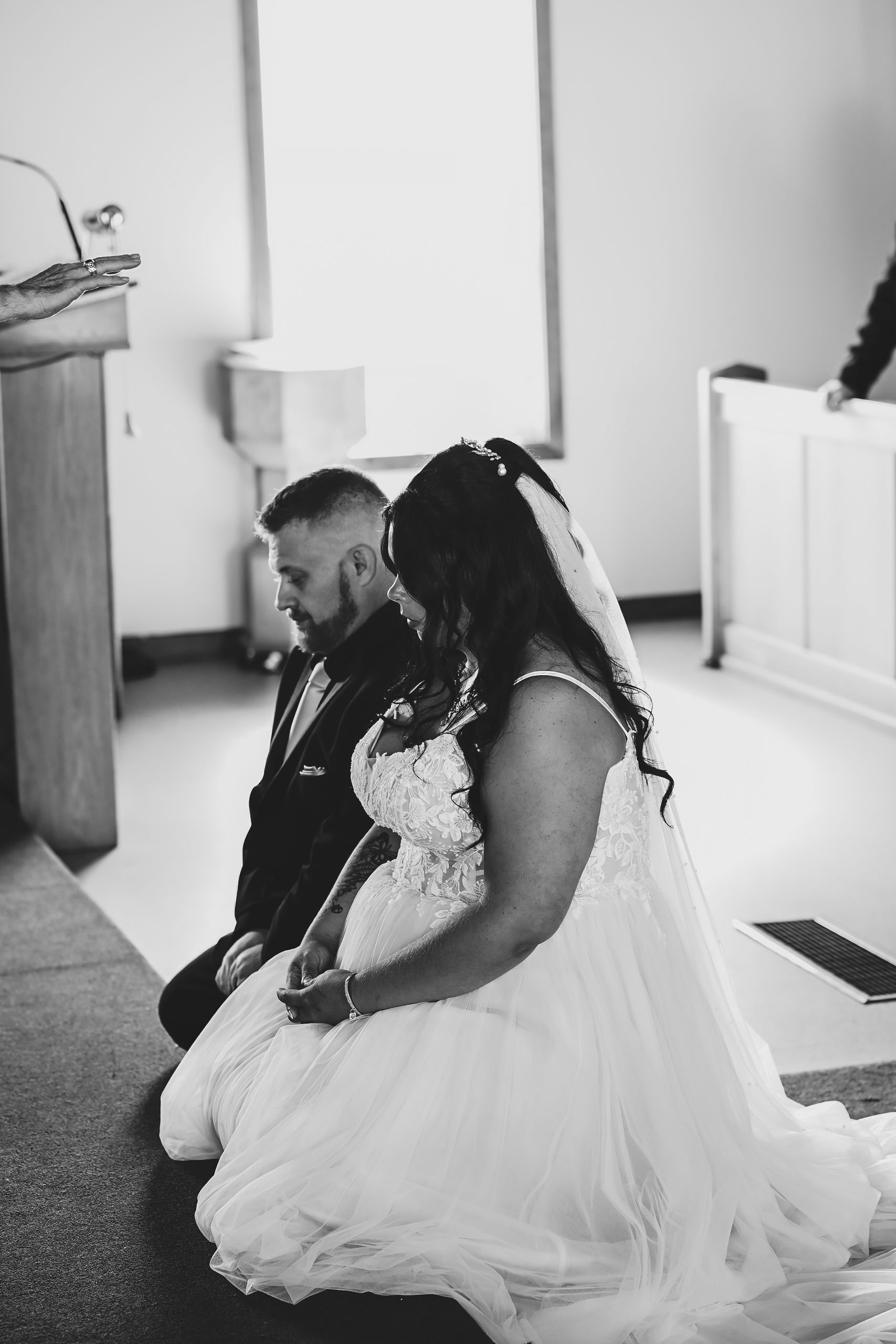 Black and white photo of the bride and groom kneeling during the church ceremony