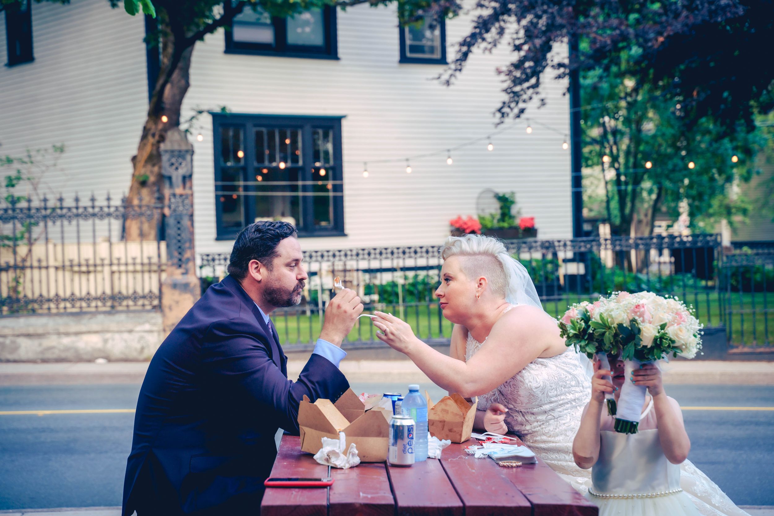 A couple taking a brief break during their wedding, with a little girl peeking out playfully, in downtown St. John’s.