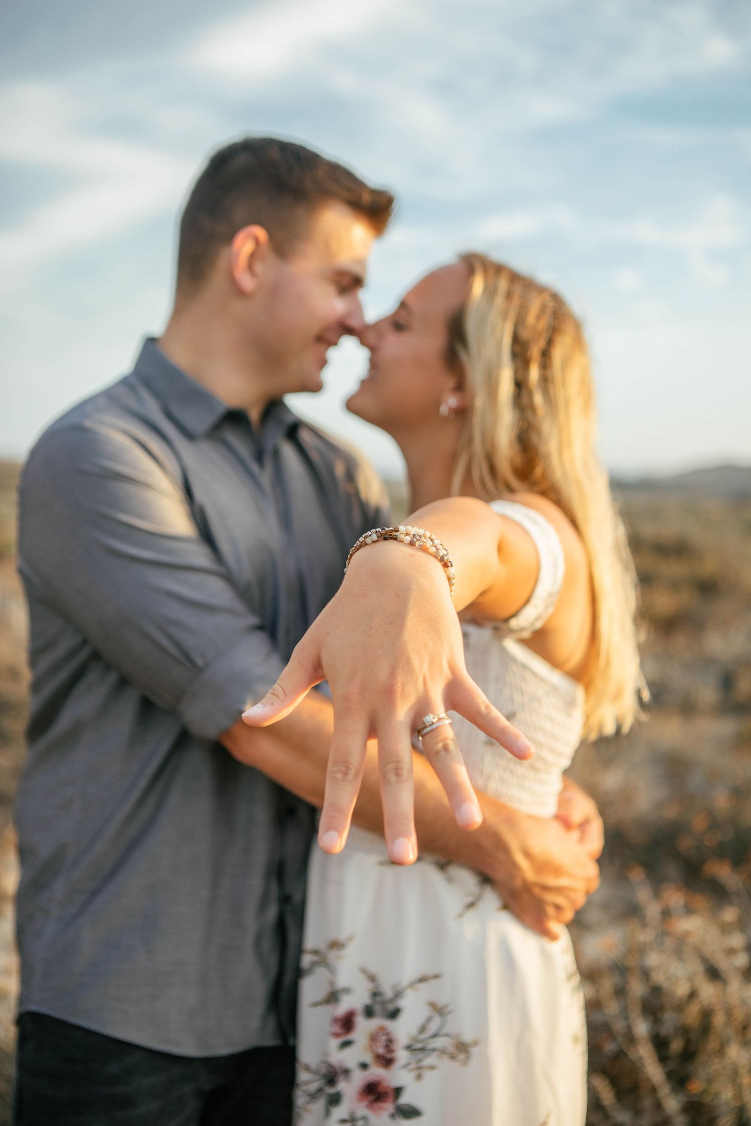 Couple showing engagement ring during sunset photoshoot in desert landscape.