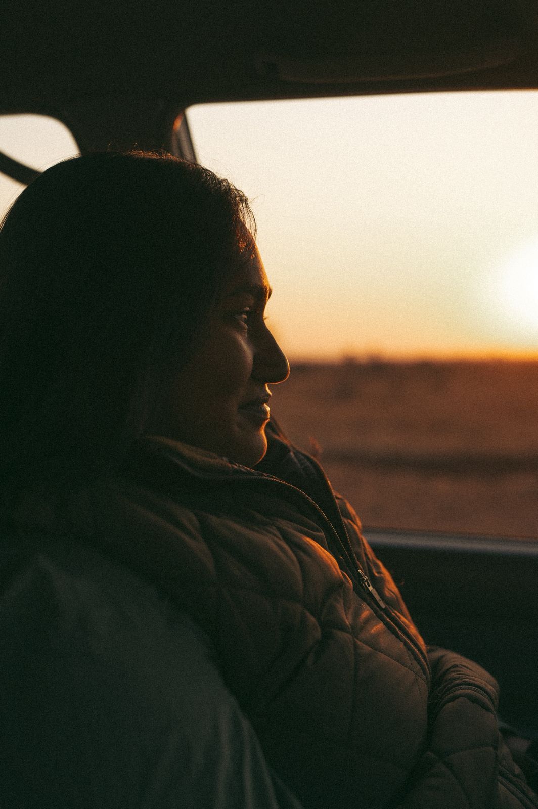 Silhouette of person gazing at golden sunset through car window.