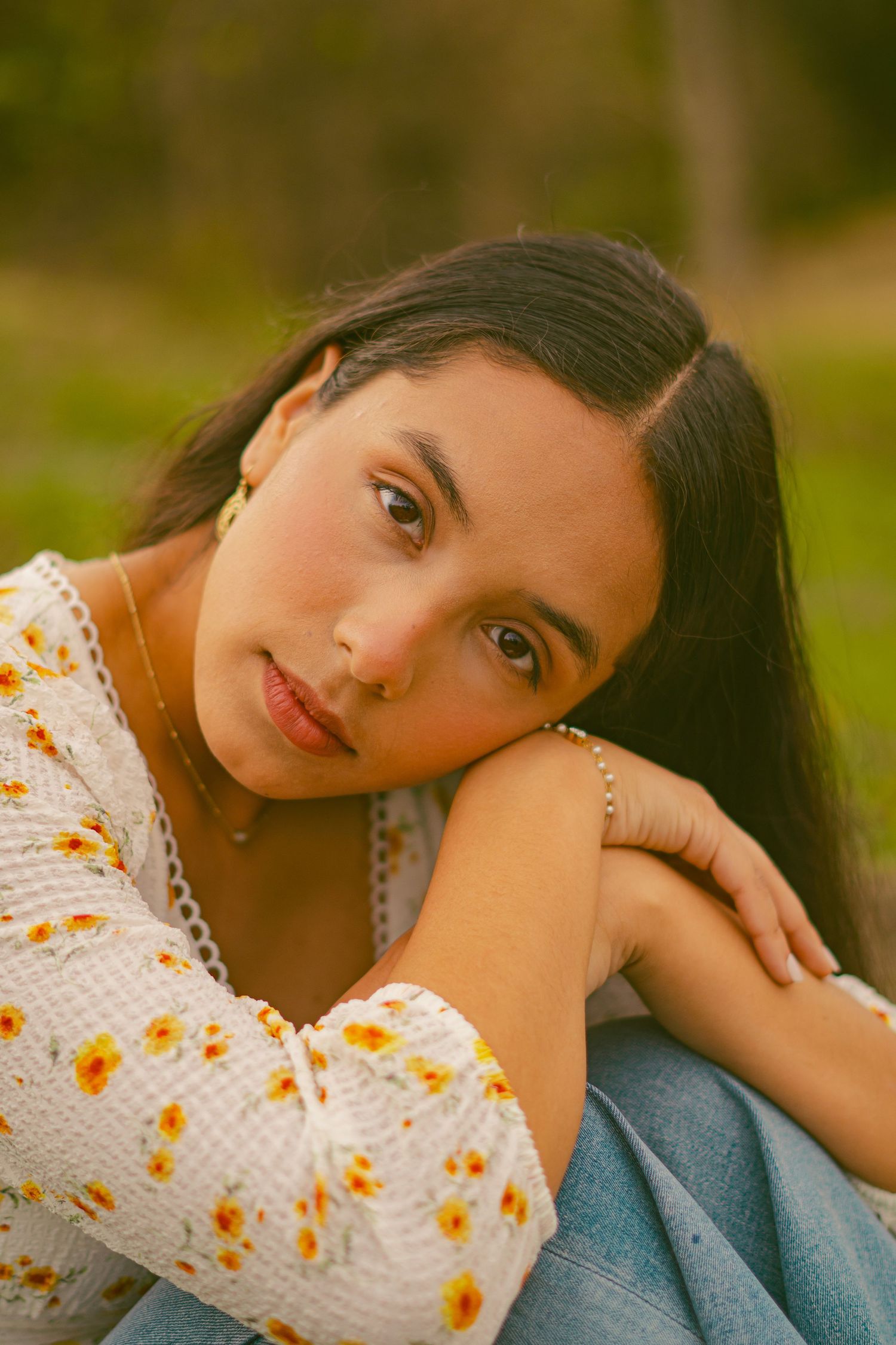 Portrait of person in floral dress resting head on knee with warm sunset lighting.