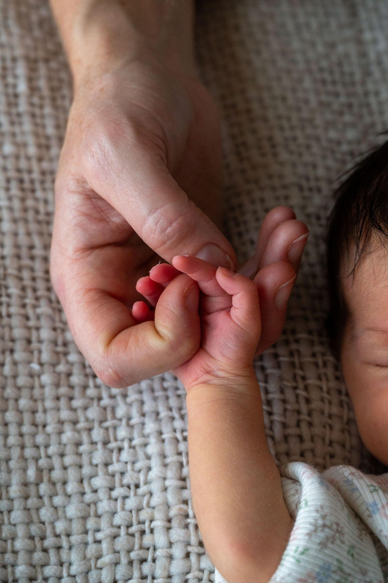 Sleeping newborn nestled in hands wearing soft white knit clothing.