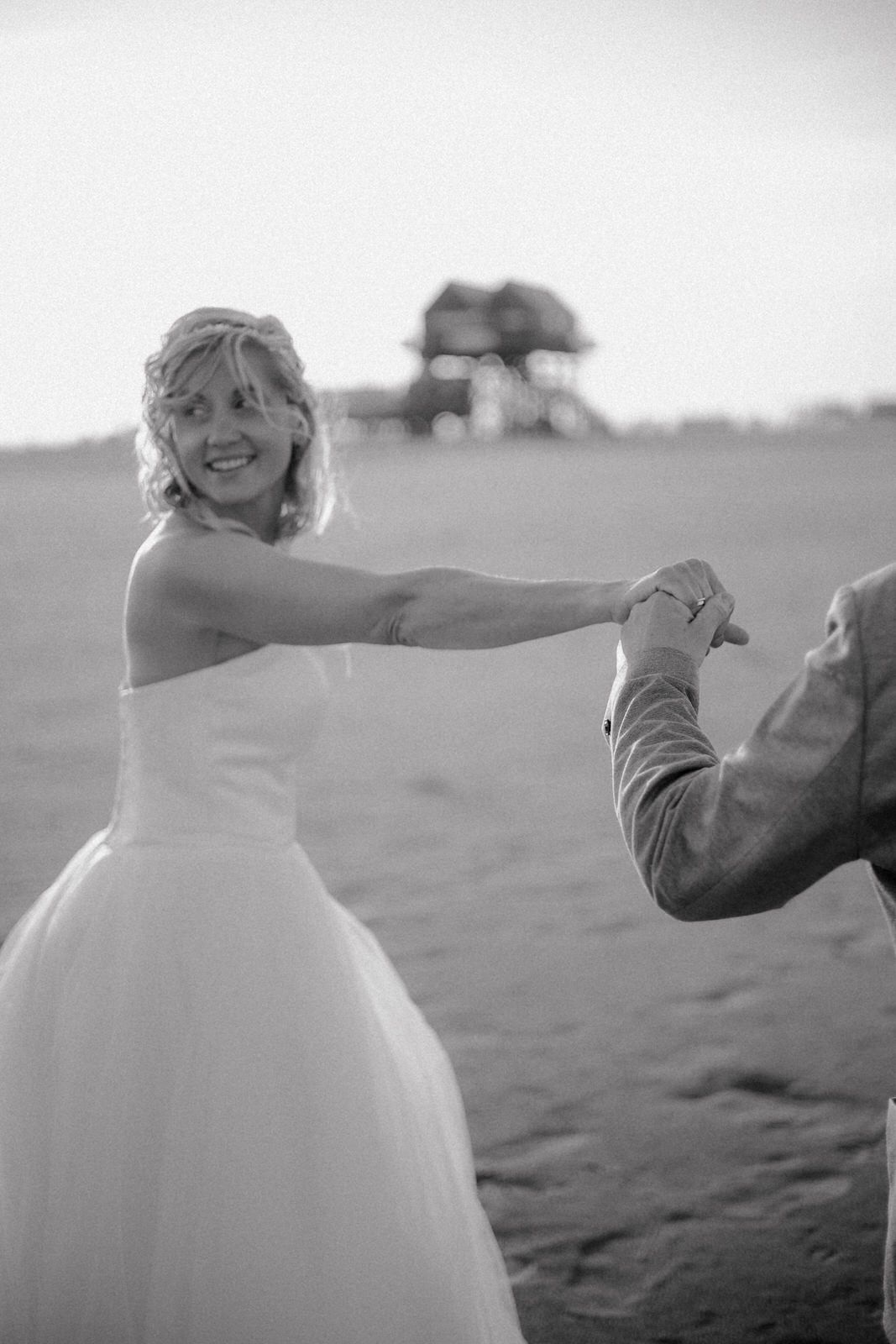 Black and white beach wedding photos show joyful moments as couple dances together in the sand at sunset.