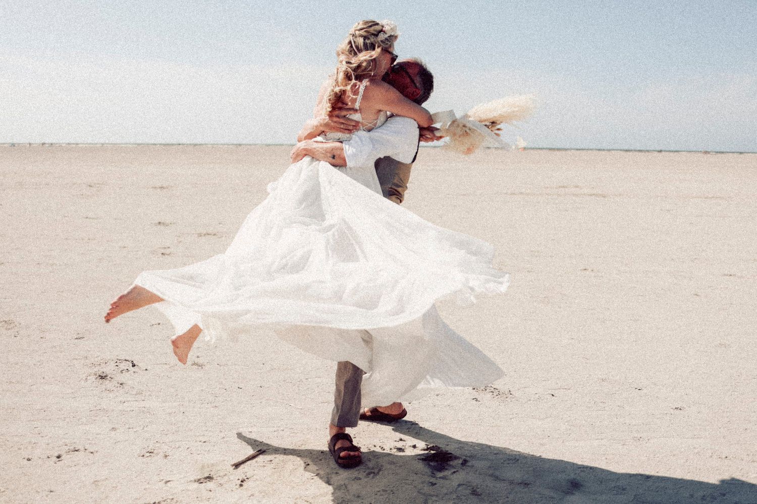 Two figures embrace in a passionate dance on a sandy beach, with a flowing white dress billowing in the ocean breeze.