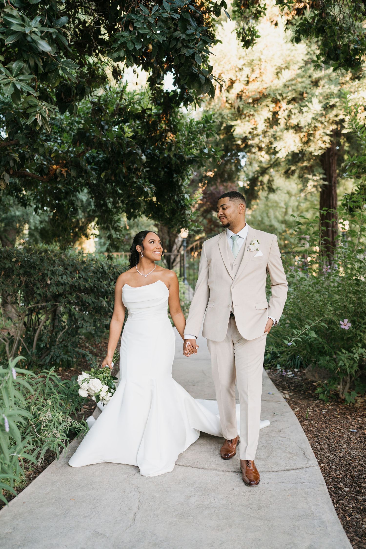 Attendants help arrange a bride's flowing veil outdoors in black and white photography.