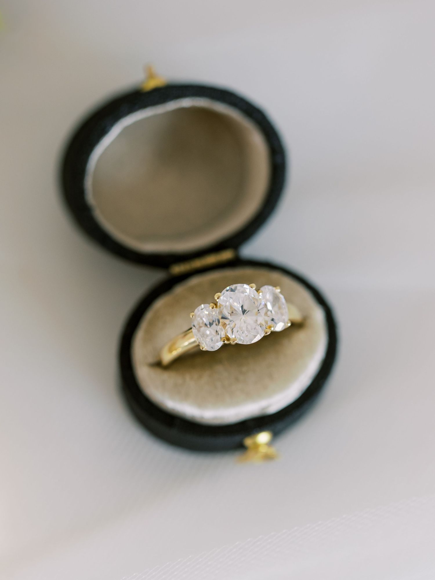 A three-stone diamond engagement ring sits in a dark velvet ring box with gold accents.
