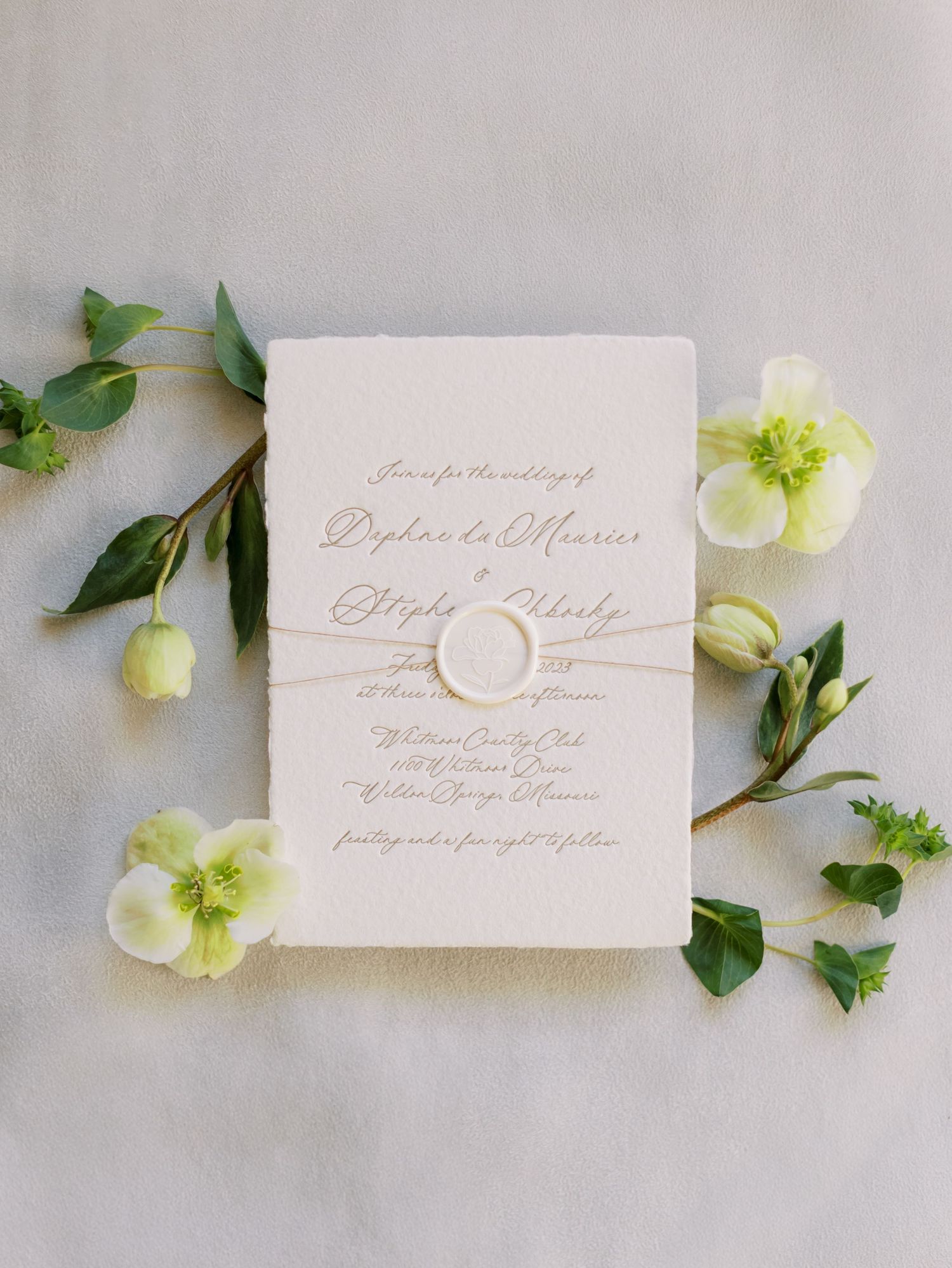 Elegant white wedding invitation with calligraphy text surrounded by delicate green hellebore flowers and foliage.