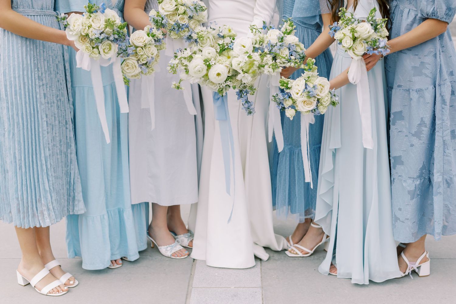 Row of bridesmaids in light blue dresses holding white and cream floral bouquets at a wedding ceremony.