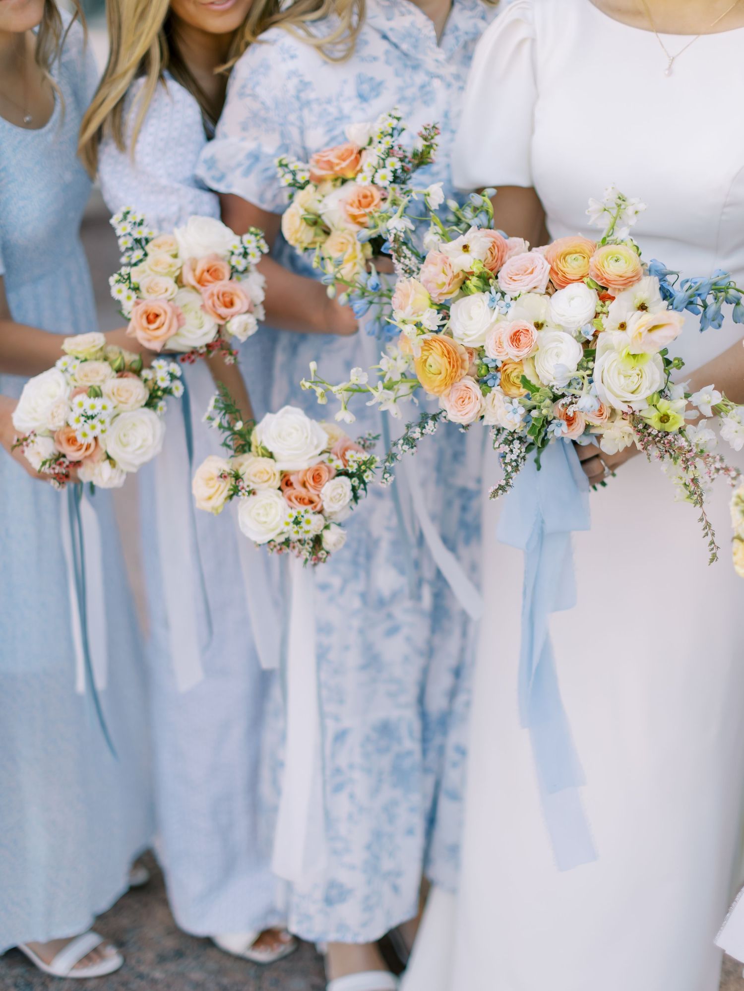 Bridesmaids in light blue dresses holding romantic peach and white floral bouquets with delicate blue accents.
