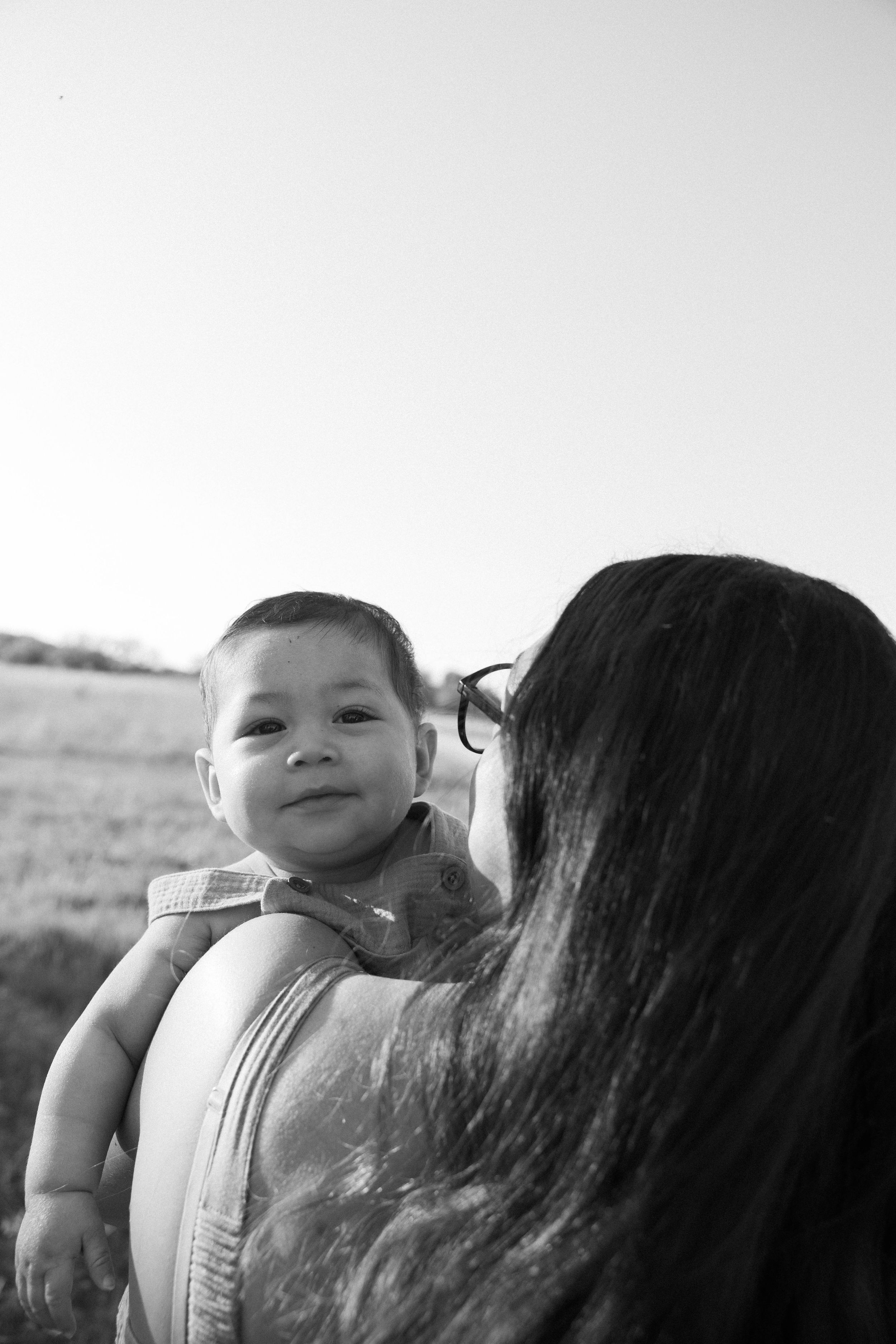 Black and white image showing a mother carrying a small child in an outdoor setting.