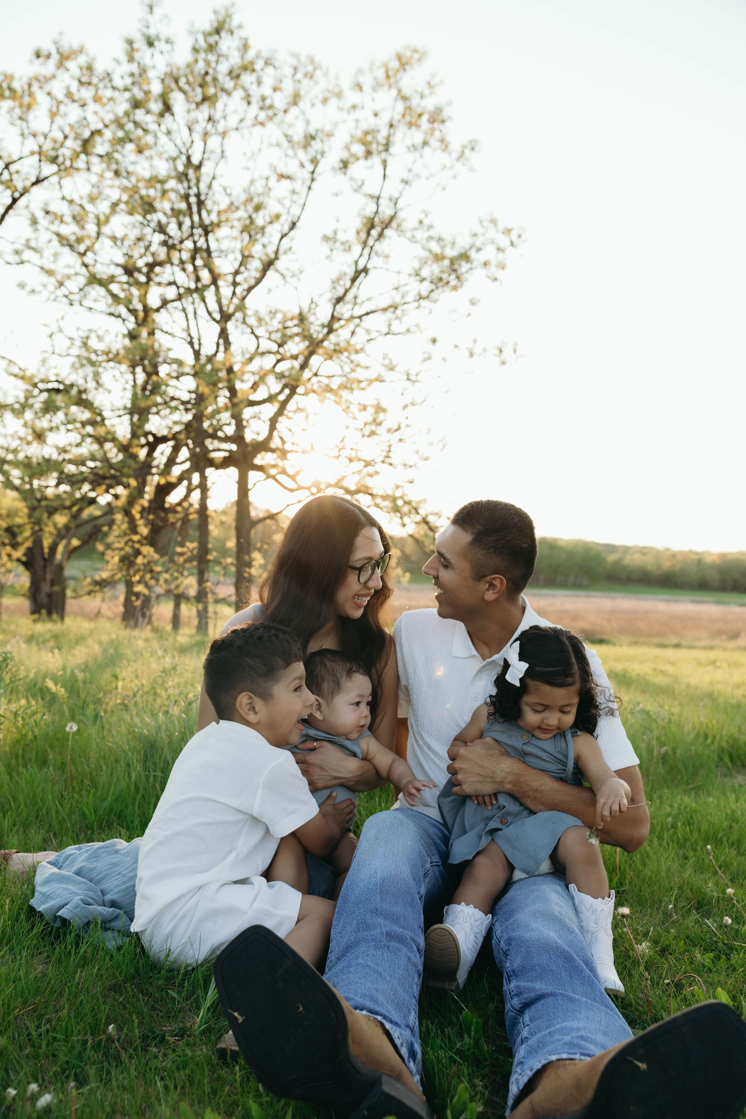 Family members laying together in a green meadow at sunset sharing tender moments in a series of connected shots.