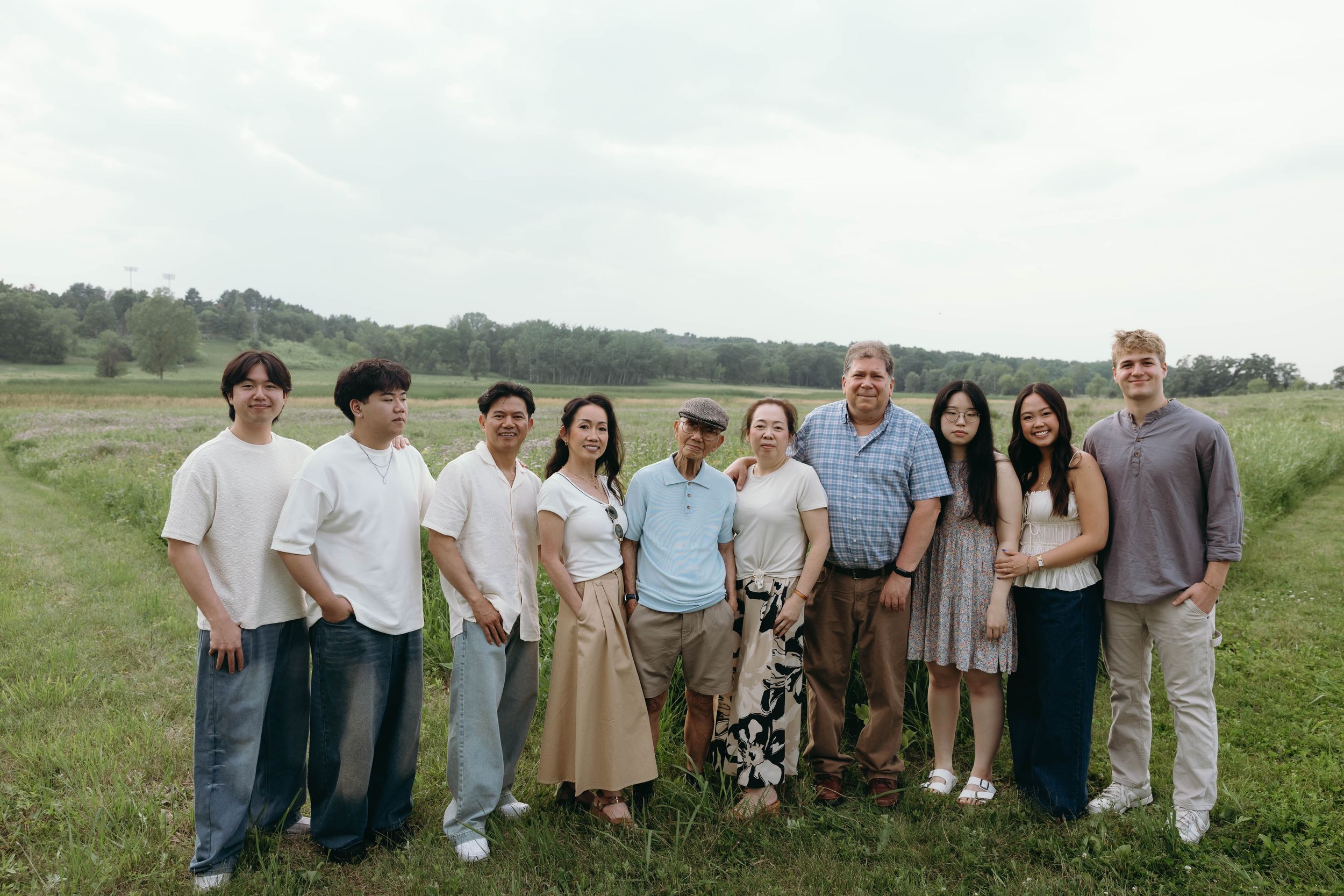 Group of people standing together outdoors in a grassy field on a partly cloudy summer day.