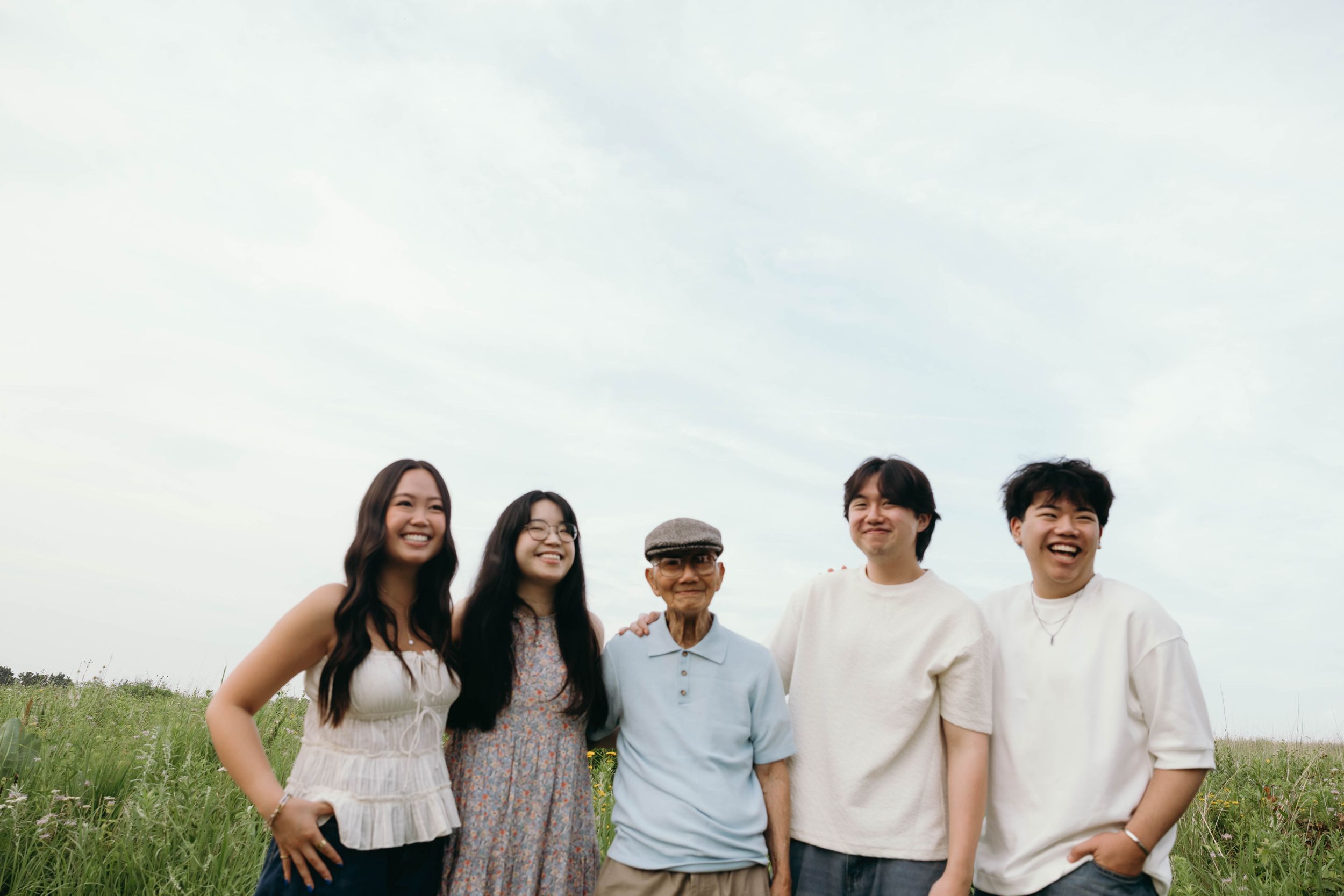 Group of friends standing together in a grassy field on a cloudy day.