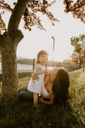 A tender sunset moment under a tree as a pair share an intimate embrace on grassy ground near a fence.