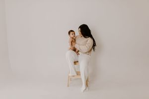 A parent and child share a sweet moment together in a minimalist white studio setting.