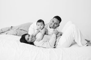 A family lounges together on white bedding sharing playful moments in black and white.