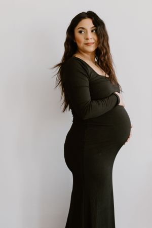 Maternity portrait of woman in black dress against white background.