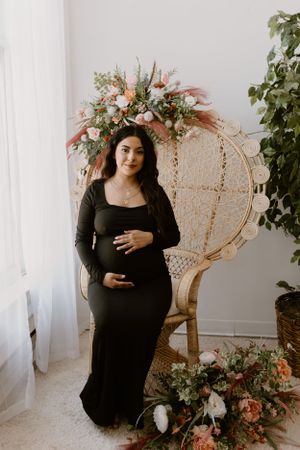 Maternity photo with floral peacock chair and decorative arrangements.