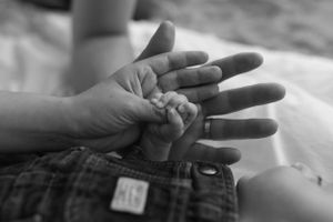 A tender black and white close-up of an adult's hand gently holding a baby's tiny hand.