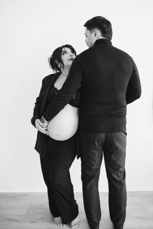 Artistic black and white maternity photo with couple in matching dark clothing.
