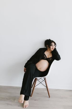 Stylish maternity portrait with mother-to-be in black attire against white wall.