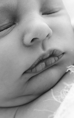 Close-up black and white photo of a sleeping newborn baby's peaceful face with delicate features.