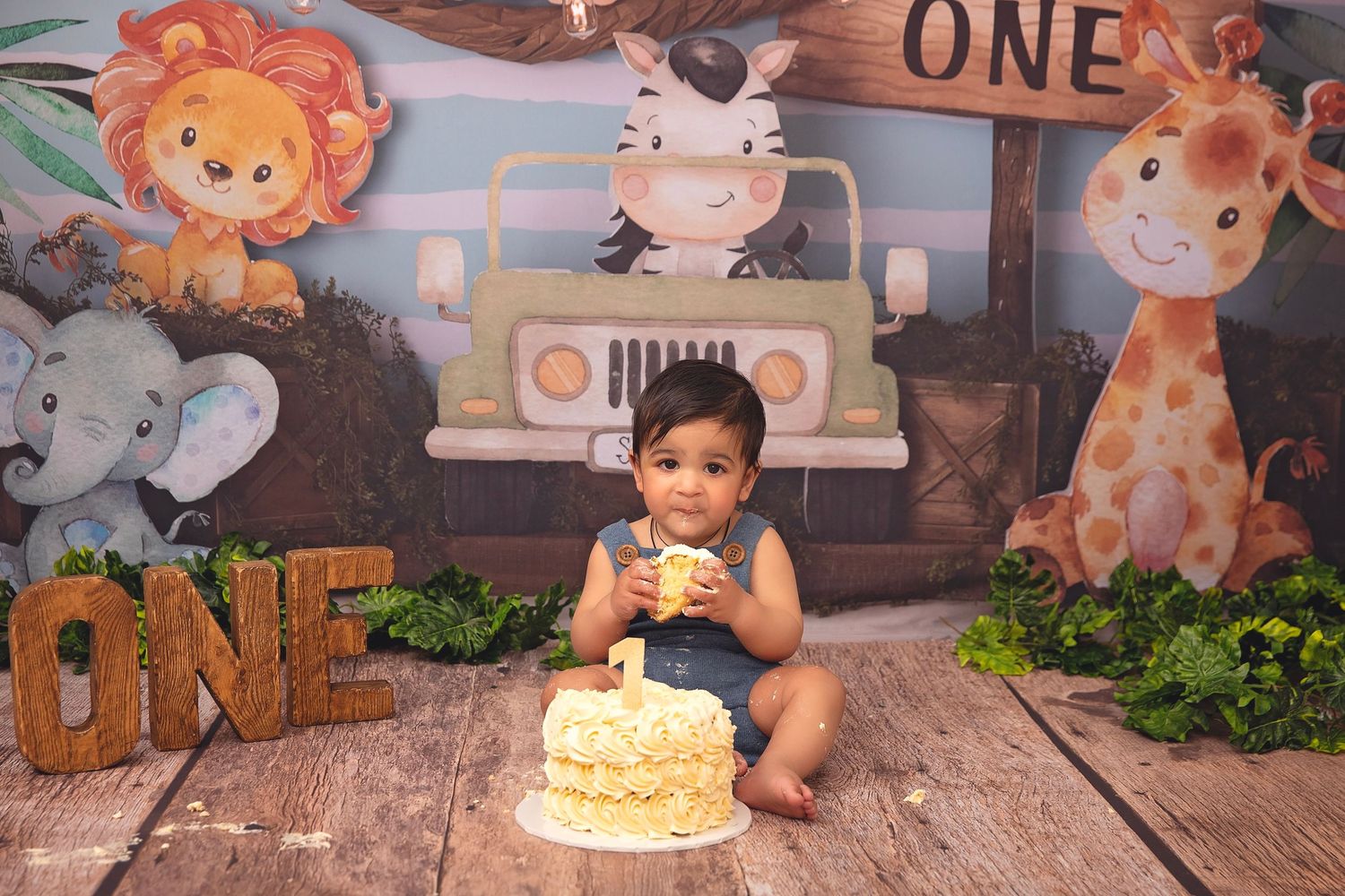 Baby boy in denim romper smashes yellow cake at safari jungle themed first birthday photo session.