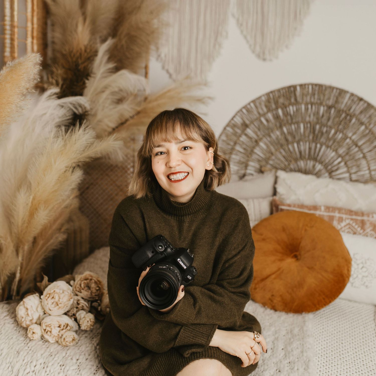 Photographer with camera in boho-styled studio with pampas grass and macrame decor.