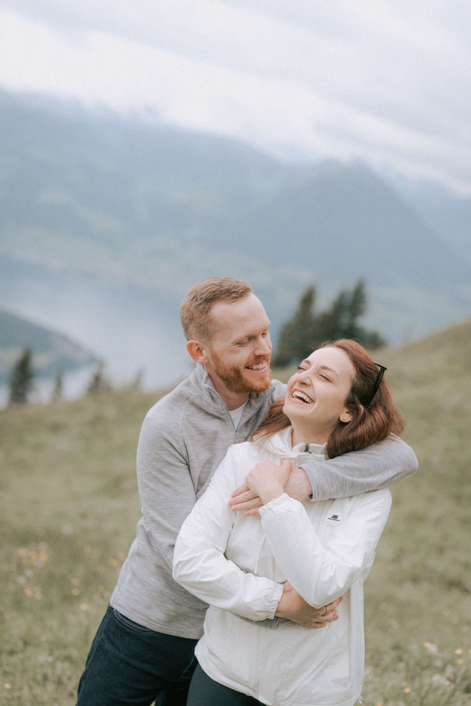 Joyful couple embracing and laughing on a green mountainside.