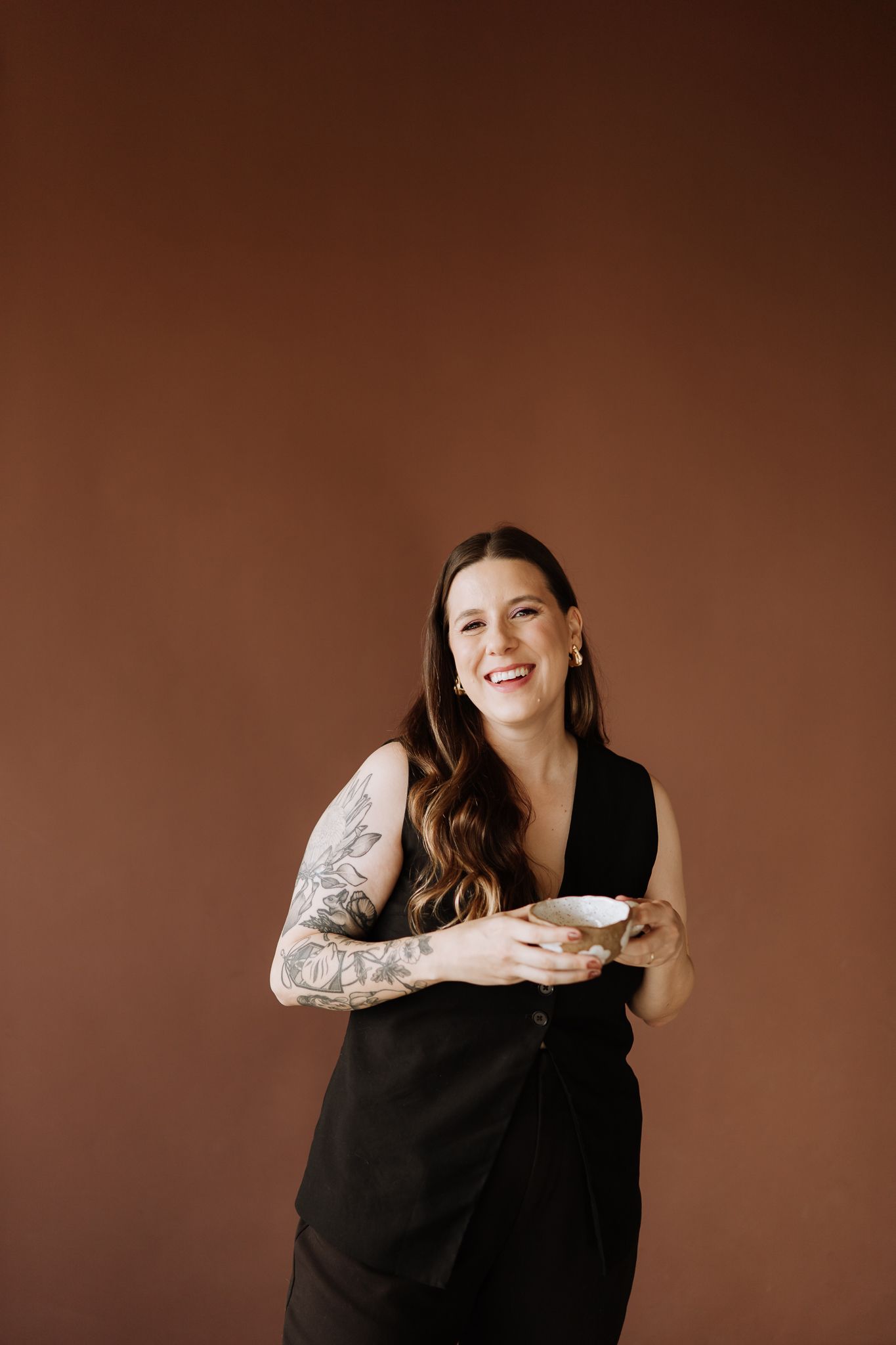 Portrait against warm brown background showing joyful expression and sleeve tattoos.