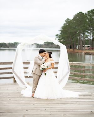 A romantic wedding ceremony on a lakeside dock with white fabric draping and pine trees in the background.