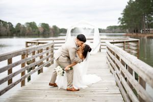 Newlyweds share a romantic dip on wooden boardwalk overlooking peaceful lake.