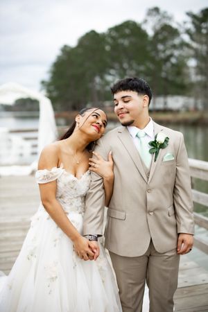 Happy wedding couple embracing on wooden pier with scenic lake view.