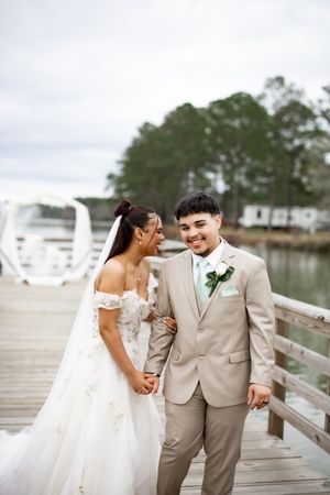 Joyful wedding couple sharing laughter on wooden dock with white arch in background.