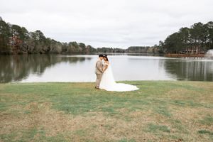 A wedding couple embracing by a serene lake surrounded by trees.