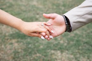 Close-up of newlyweds holding hands showing wedding rings against a blurred natural background.