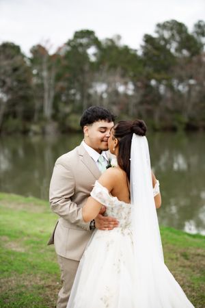 Wedding couple shares a tender embrace by a serene lake with pine trees in the background.