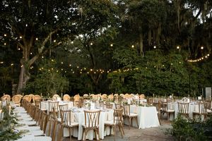 Elegant outdoor wedding reception setup with white tables and chairs under string lights in a lush garden setting.
