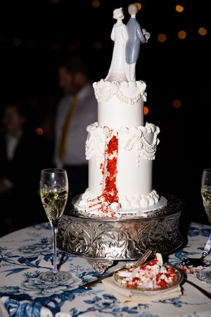 A white wedding cake with red splatter design on a silver cake stand creates a dramatic Halloween-inspired effect.