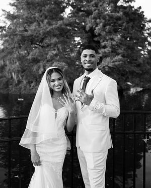 A joyful couple in matching white outfits share candid moments during their wedding photoshoot outdoors.