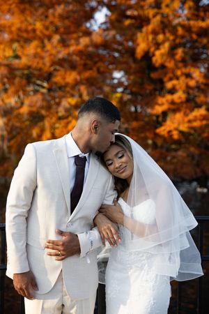 A romantic autumn wedding photo series showing a couple in white attire embracing against vibrant orange fall foliage.