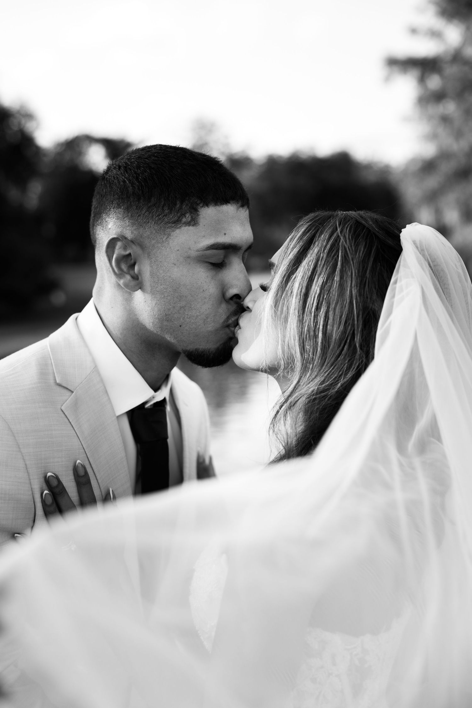 A romantic black and white wedding photo showing a tender kiss through a flowing white veil.