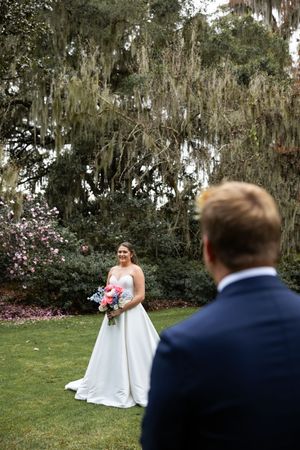 A wedding first look sequence shows the bride in a white dress surprising the groom in a navy suit in a garden setting.