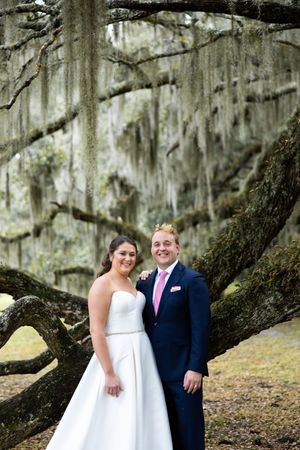 A couple poses together under Spanish moss draped trees in a romantic outdoor setting.