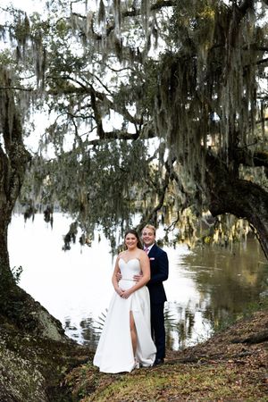 A couple poses for romantic wedding photos under moss-draped oak trees beside a serene lake in the Southern outdoors.