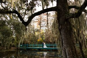 Spanish moss hanging from oak trees frames a turquoise bridge in a romantic garden setting.