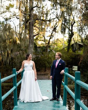 Wedding couple walking along a turquoise bridge surrounded by Spanish moss-draped trees.