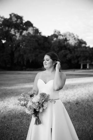 Black and white wedding photo showing a bride in a strapless dress holding a floral bouquet in an outdoor setting.